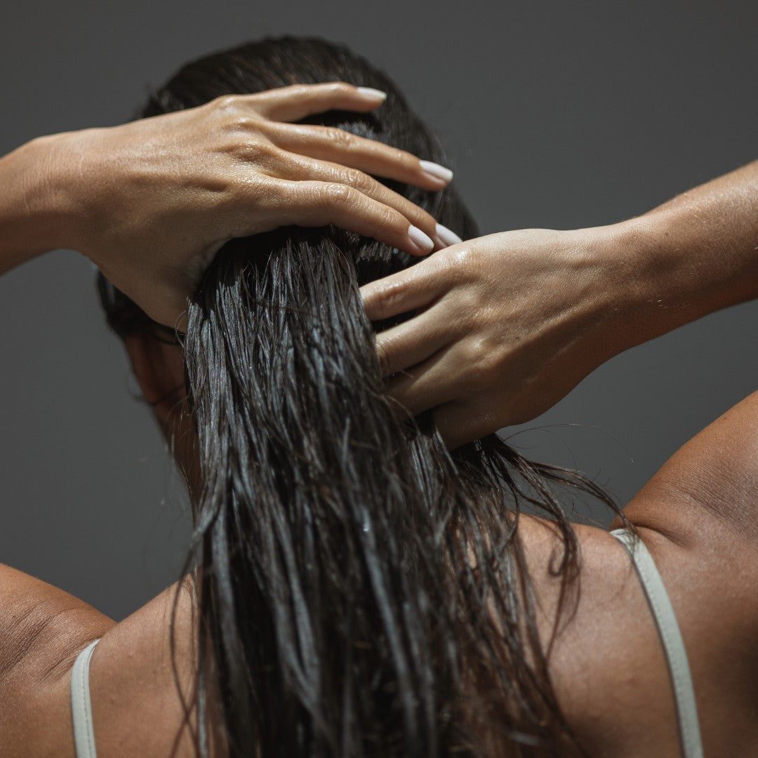 Person washing hair with hands against a dark background