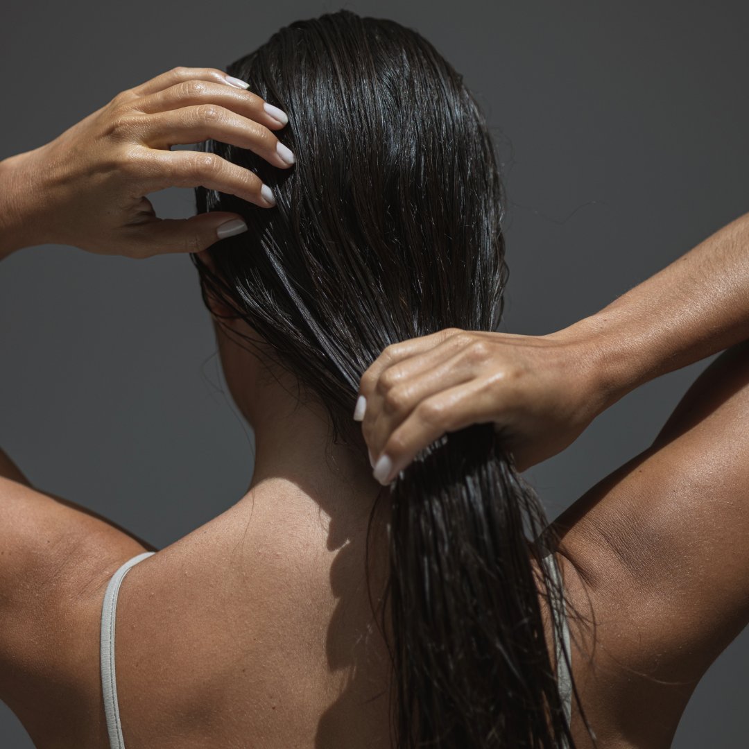 Person with long dark hair being styled against a gray background
