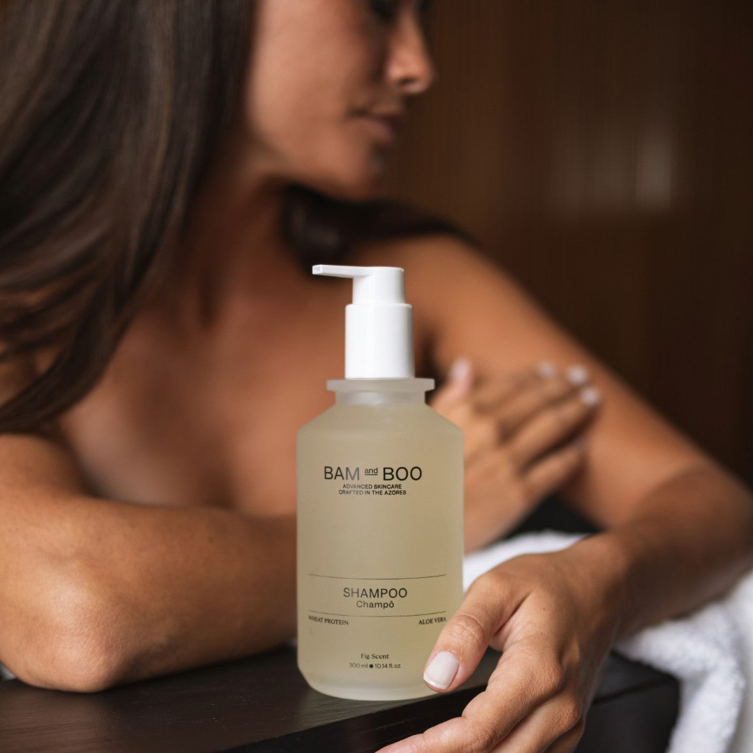 BAM BOO shampoo bottle held by a person with a blurred background. Minimalist premium amenities with botanical ingredients.