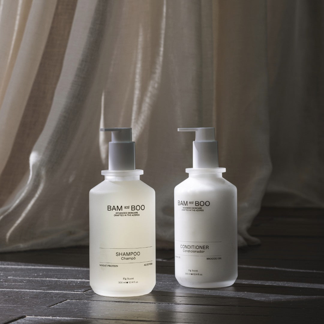 BAM and BOO shampoo and conditioner bottles on a wooden surface with a neutral curtain background. Sustainable amenities collection with shampoos, shower gels, and lotions.