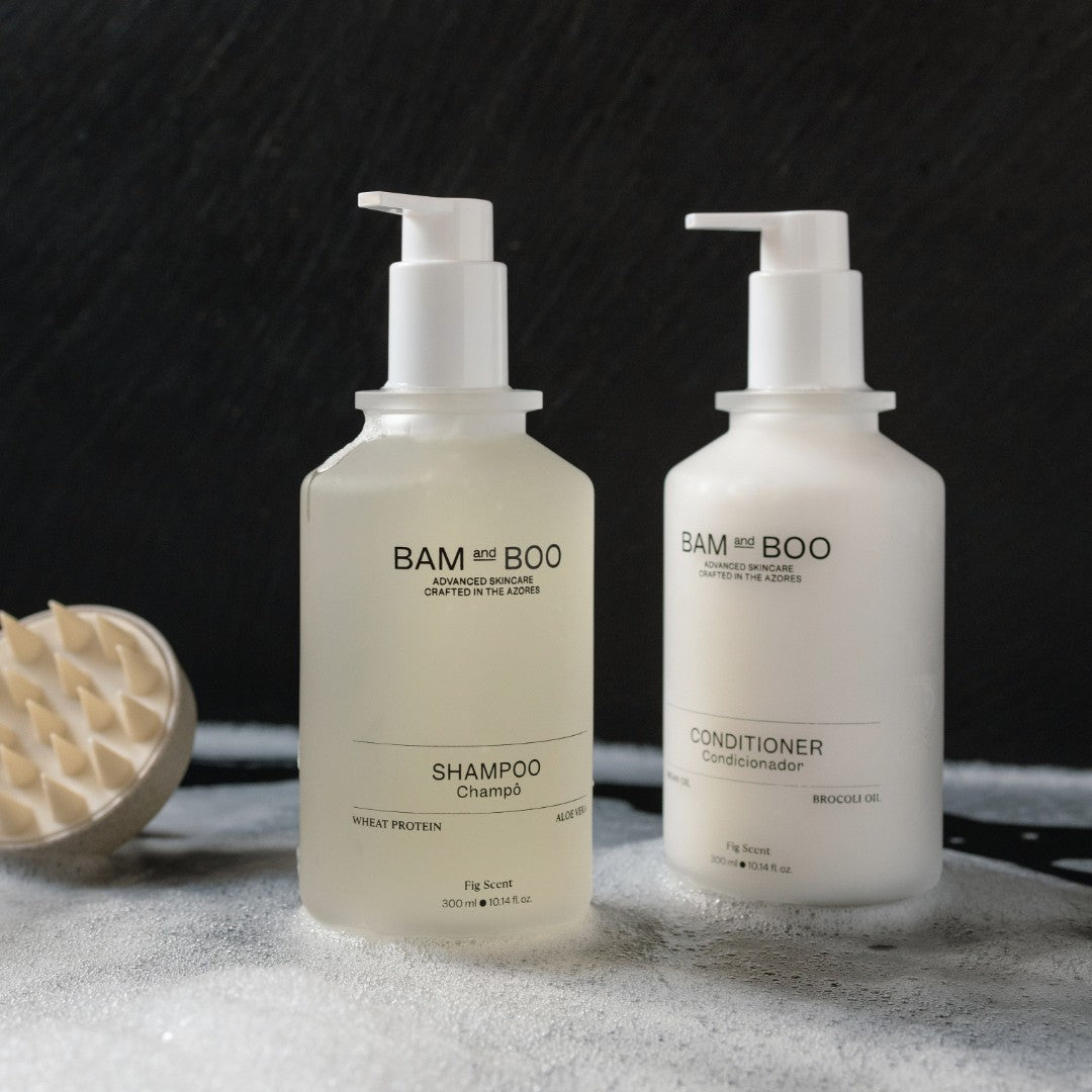 Two bottles of BAM & BOO shampoo and conditioner on a textured surface with a black background. Natural premium amenities made in portugal for home hotels and spa